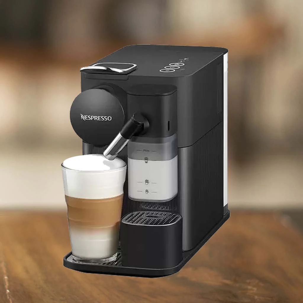 A imagem é composta pela cafeteira Nespresso Lattissima one de cor preta e sob uma mesa de madeira. Há nessa cafeteira de cápsula um copo contendo um capuccino. Nespresso com Luzes Vermelha ou Laranja Piscando