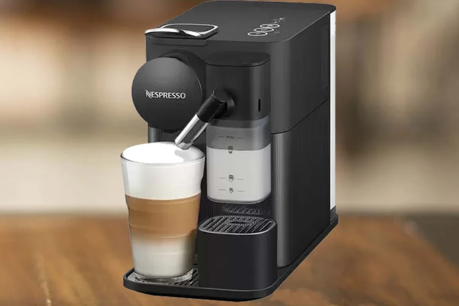 A imagem é composta pela cafeteira Nespresso Lattissima one de cor preta e sob uma mesa de madeira. Há nessa cafeteira de cápsula um copo contendo um capuccino