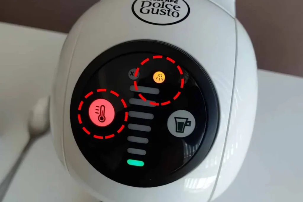 A imagem contém a Dolce Gusto Genio branca com alerta de descalcificação de cor laranja ativado, bem como acesa o botão de temperatura na cor vermelha. Foi destacado essas duas luzes com uma circunferência pontilhada de cor vermelha. Post luz laranja, amarela ou vermelha acesa ou piscando na cafeteira de cápsulas Dolce Gusto.