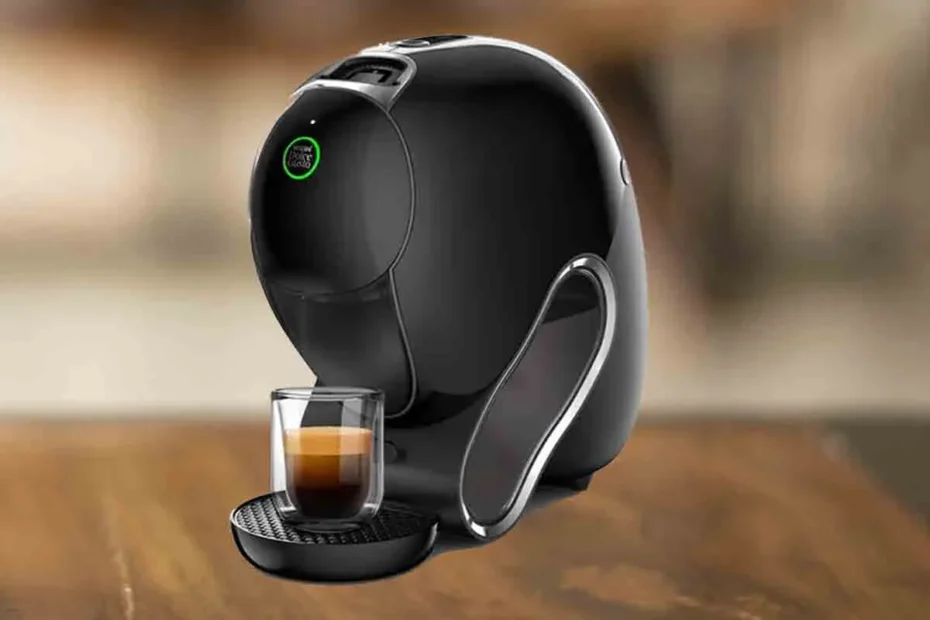 Para ilustrar a postagem "Dolce Gusto Neo Vale a pena" a imagem é composta pela cafeteira de cápsulas Dolce Gusto Neo de cor preta com um copo com café dentro. Essa cafeteira está em uma mesa de madeira e o resto do fundo está desfocado.