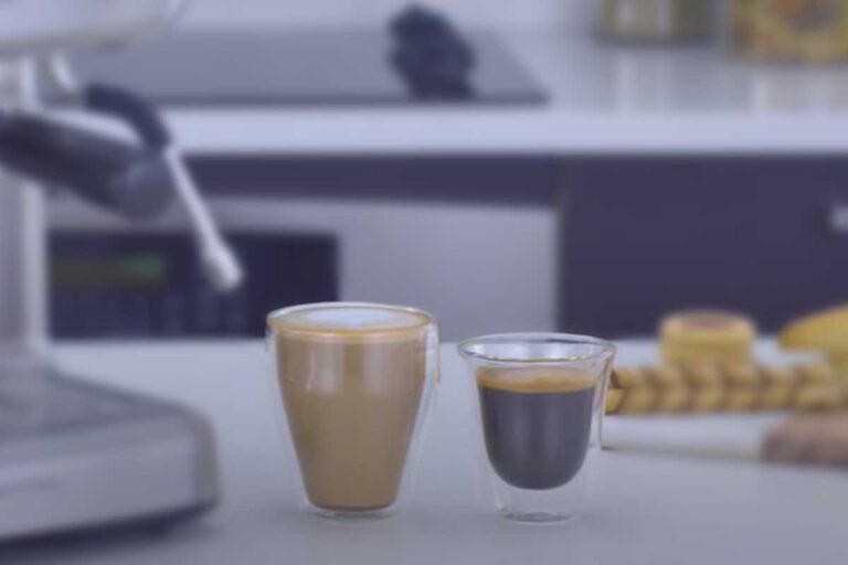 lateral de uma máquina de café expresso sem detalhes de marca ou modelo. 1 copo bem cheio de capuccino e outro com café expresso