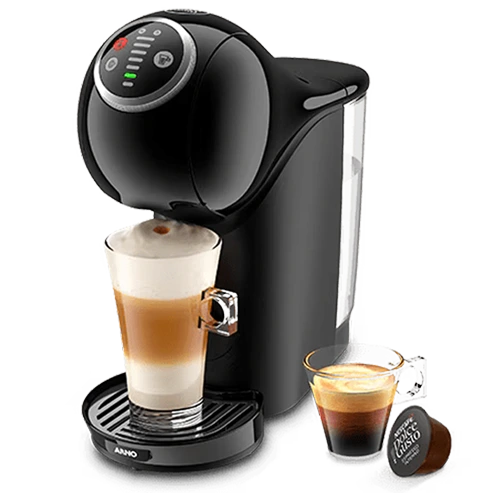 A imagem contém a cafeteira Genio S Plus da Dolce Gusto. A cor predominante dessa cafeteira expresso é preto. Há uma xícara com café e uma cápsula ao lado cafeteira. Na cafeteira há um copo de cappucino sendo preparado.